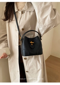 Detail of black lychee grain bucket bag featuring a gold metal clasp and leather strap