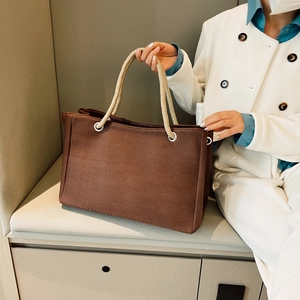 Detail of dark brown canvas tote bag with woven rope handles worn by a woman