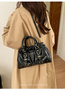 Detail of black glossy tote bag with vintage pleats and gold hardware on person