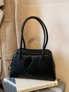 Classic black leather Boston bag with long handles placed on a silver suitcase