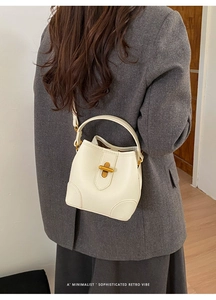 Detail of cream lychee leather bucket bag with gold cross-lock buckle on a model