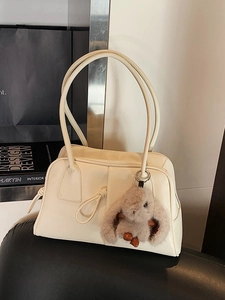 Stylish cream shoulder bag with brown plush bunny charm on a black leather chair