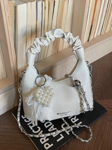 White ruched handbag with pearl heart pendant and metal chain strap on books