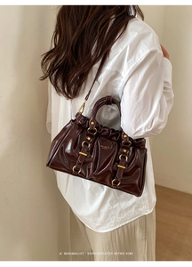 Detail of burgundy tote bag showing vintage pleats and gold hardware on model