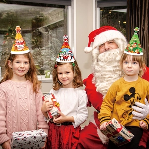 Three kids wearing paper Christmas party hats with 3D gingerbread and penguin toppers