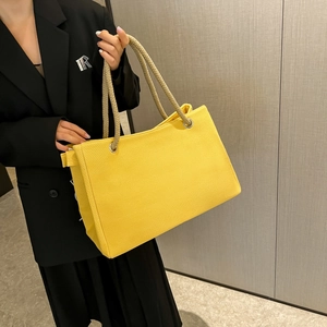 Detail of a bright yellow tote bag featuring thick khaki woven rope handles and silver rings