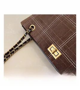 Close-up of golden metal twist lock and white grid stitching on brown suede tote bag