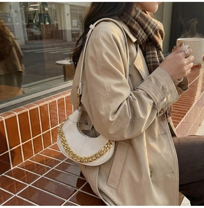 Détail d'un sac demi-lune beige avec chaîne dorée porté par une femme en trench-coat chic