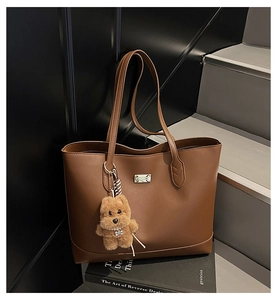 Detail of brown PU leather tote bag with silver logo plaque and plush bear charm