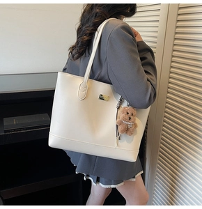 Detail of a beige tote bag with gold metal plate and brown plush bear charm accessory