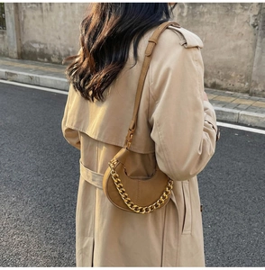 Sac demi-lune marron avec chaîne dorée porté avec un trench-coat beige élégant