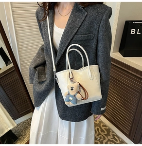 Détail d'un sac seau blanc en cuir avec un charmant ours en peluche sur un modèle élégant