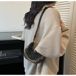 Détail d'un sac demi-lune noir avec chaîne dorée porté par un mannequin femme