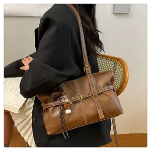 Macro detail of brown leather tote bag featuring metal buckles and decorative charm