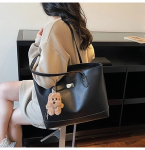 Detail of black tote bag with silver logo plaque and plush bear charm on soft leather
