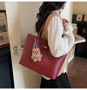Detail of red leather tote bag with a cute brown plush dog charm hanging on the side