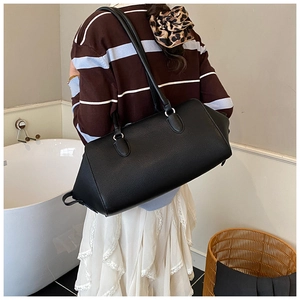 Minimalist black leather bowling bag with lychee texture shown as a shoulder carry style