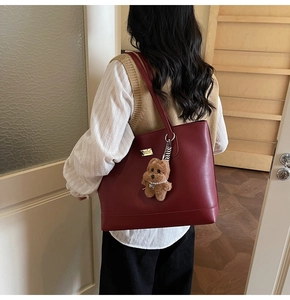 Detail of burgundy leather tote bag with a golden nameplate and plush bear charm