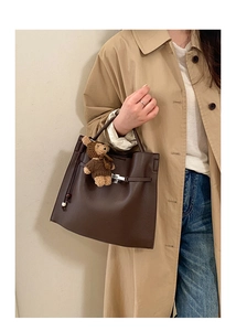 Detail of dark brown lychee leather tote bag with buckle strap and plush bear charm