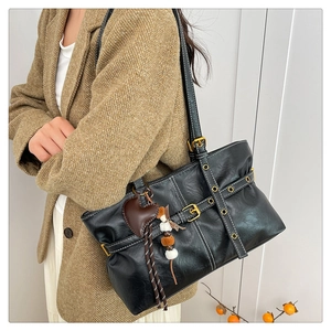 Detail of black PU leather tote bag with gold buckles and heart charm on a model