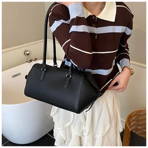 Detail of black pebbled leather handbag with long handles shown in a lifestyle setting