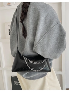 Detail of black glossy pleated shoulder bag with silver chains and leather strap