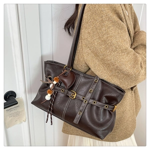 Detail of dark brown tote bag featuring heart pendant and metallic eyelet belt accents