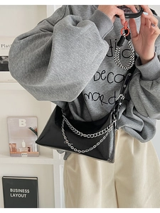 Detail of glossy black crescent shoulder bag with double silver chains and wide strap
