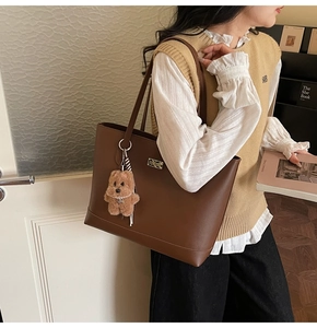 Detailed view of brown leather tote bag with gold nameplate and cute bear pendant charm