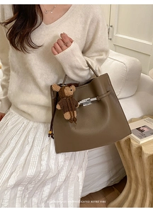 Detail view of dark brown pebbled leather tote bag with metal buckle and bear charm