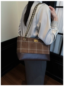 Detailed view of tote bag featuring plaid fabric, brown leather, and gold twist lock