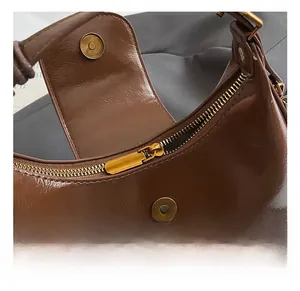 Detail showing the golden metal zipper and magnetic buckle on dark brown crescent bag