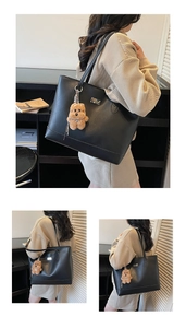 Detail of black leather tote bag with cute plush bear charm and metallic logo plaque