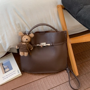 Detail of dark brown pebble leather handbag with silver lock and plush bear charm