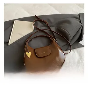Detail of brown half-moon crossbody bag with gold heart charm and glossy finish