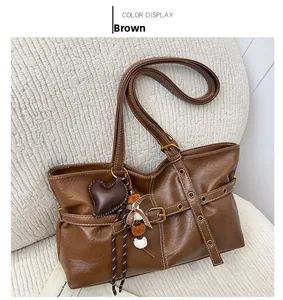 Detailed view of a brown tote bag with heart charm, plush ball, and vintage buckle accents