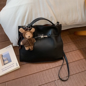 Detail of black lychee grain handbag with silver clasp and brown bear plush charm
