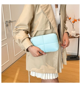 Close-up of light blue quilted puff makeup bag held by model wearing a beige trench coat
