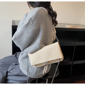 Detail of off-white lychee leather texture and silver chain strap on a crossbody bag