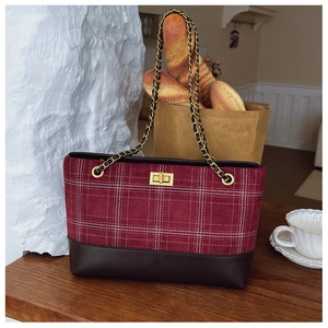 Detail of red plaid tote bag with dark brown leather base and gold chain strap