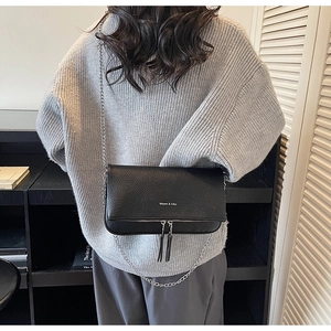 Close-up of black lychee grain leather crossbody bag with dual tassel zipper details