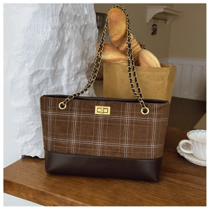 Close-up of brown plaid tote bag with golden twist lock and chain strap on wood table