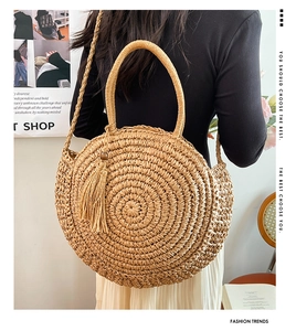 Round woven straw bag with tassel detail and crossbody strap shown in a lifestyle scene