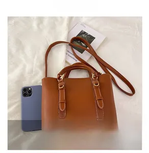 Brown leather bucket bag with top handles and shoulder strap shown with smartphone for size