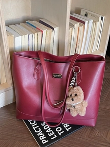 Large burgundy leather tote bag with a teddy bear charm against a cozy library background