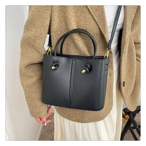 Detail einer schwarzen Leder-Beuteltasche mit goldenen Beschlägen zum braunen Blazer