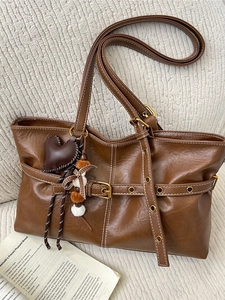 Vintage brown leather tote bag with contrast stitching and decorative charms on a desk