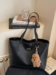 Minimalist black leather tote bag with a cute plush bear pendant on a white shelf