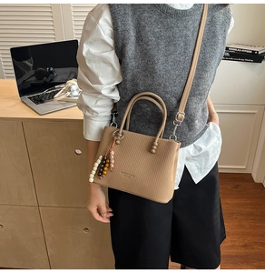 Detail of light brown tote bag with vertical stripes, bead tassel, and shoulder strap
