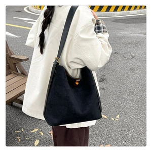 Outdoor shot of a black suede tote bag with wide strap and gold hardware on model's shoulder